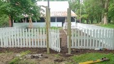 a white picket fence in the middle of a yard next to a house and trees