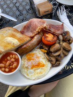 a white plate topped with eggs, bacon, toast and other breakfast foods on top of a table