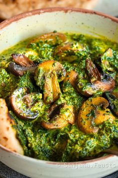 a white bowl filled with mushrooms and pesto on top of a table next to bread