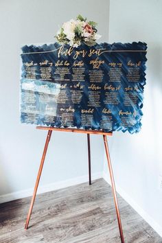 a wedding seating chart with flowers on top is displayed in front of a white wall