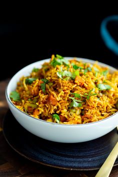 a white bowl filled with rice and veggies on top of a wooden table