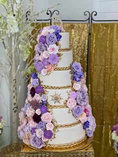 a three tiered wedding cake with purple and pink flowers on the top, surrounded by gold sequins