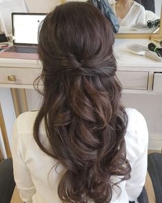 a woman sitting at a desk with her hair in a half updo and curls