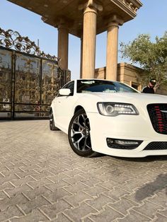 a white car parked in front of a tall building with columns on it's sides