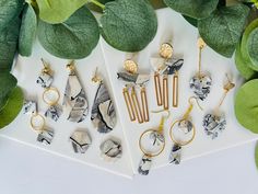 several different types of earrings on display next to green leafy plants and white paper