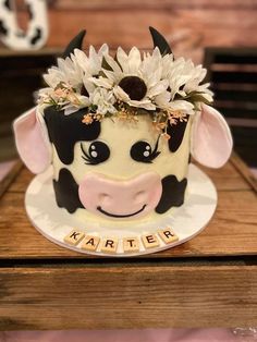 a cow cake with flowers on it sitting on top of a wooden table in front of a sign