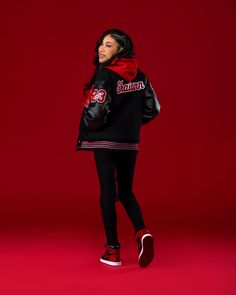 a woman in black jacket and red scarf standing against a red background with her hands on her hips