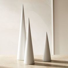 three white vases sitting next to each other on top of a wooden table in front of a wall