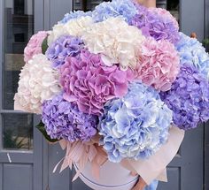 a woman holding a large bouquet of purple and white flowers in front of a door