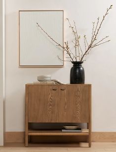 a vase with some flowers sitting on top of a wooden cabinet next to a painting