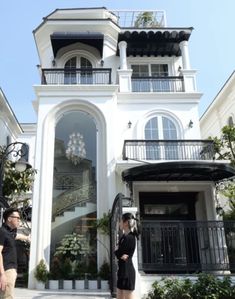 two people standing in front of a large white building with black balconies on it