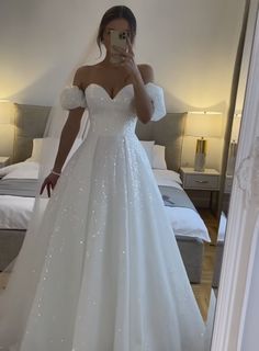 a woman in a wedding dress taking a selfie with her cell phone while standing in front of a bed