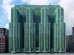 a large green building sitting in the middle of a city with tall buildings behind it