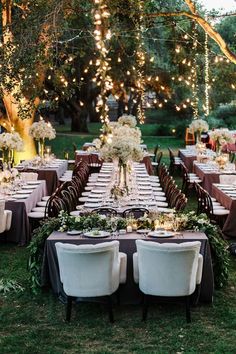 an outdoor dinner table set up with white flowers and greenery on the tables, surrounded by string lights