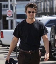 a young man walking down the street with his hat in his hand and sunglasses on