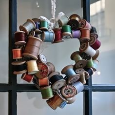 a heart shaped wreath made out of spools of thread on a window sill