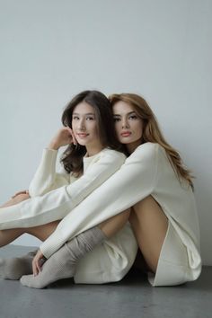 two women sitting on the ground with their arms around each other, both wearing white sweaters and knee high socks