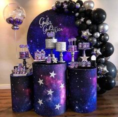 a table topped with cakes covered in purple and black stars next to balloons on top of a wooden floor