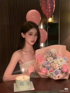 a woman sitting at a table with a birthday cake and flowers in front of her