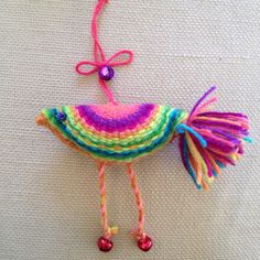 a crocheted bird ornament hanging on a white surface with pink, yellow, green, and blue yarn