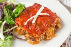 a white plate topped with lasagna next to a green leafy vegetable salad