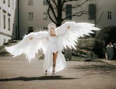 a woman with white wings walking down a street