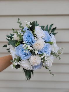 a bouquet of blue and white flowers is held by someone's hand in front of a house