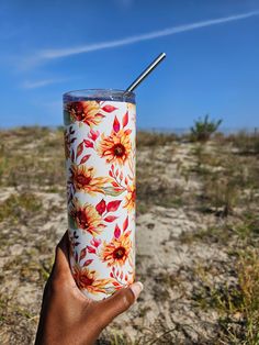 a person holding up a cup with a straw in it on the desert ground and blue sky