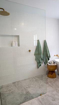 a bathroom with a glass shower door and white tile walls, along with a wooden stool in front of the bathtub