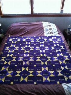 a bed with a purple and yellow quilt on it's side next to a window