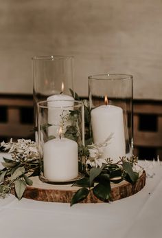 three candles sitting on top of a wooden slice with greenery and flowers around it