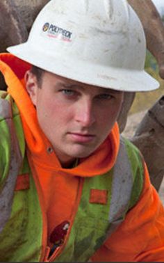 a man in an orange and green jacket wearing a hard hat next to a horse