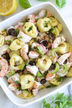 a white bowl filled with pasta and shrimp on top of a table next to lemon wedges