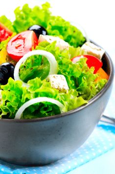 a salad with lettuce, tomatoes and olives in a metal bowl on a blue napkin