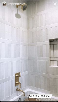 a bathroom with white tile and gold faucet in the bathtub next to a window