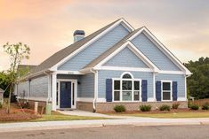 a blue house with white trim and shutters on the front door is shown at sunset