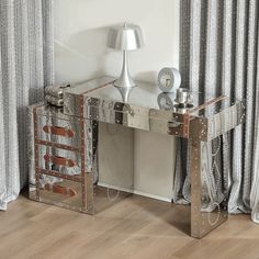 a mirrored console table with two drawers and a lamp on top, in front of a curtained window