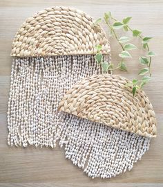 two pieces of woven material sitting on top of a wooden table next to a plant