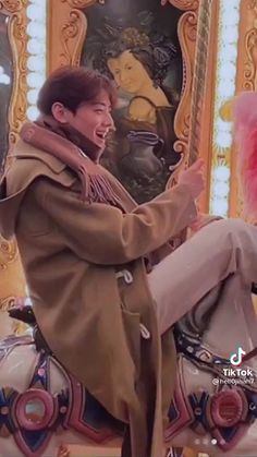 a man sitting on top of a merry go round with a pink pom - pom