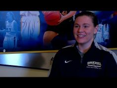 a female basketball player is smiling in front of a wall with sports pictures on it