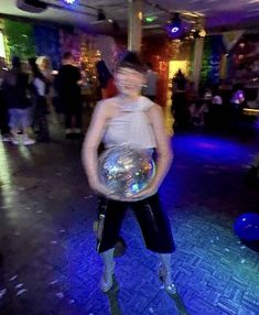 a woman is holding a disco ball in her hands while standing on the floor with other people