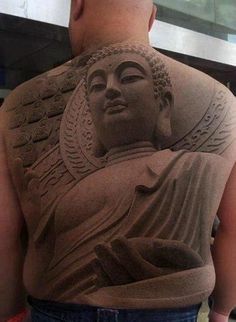 the back of a man's body is covered in sand and has a buddha statue on it