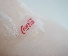 the coca cola logo is red and white on top of a soft material sheet with water droplets around it