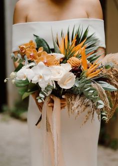 a woman wearing a white dress holding a bouquet with orange and white flowers on it