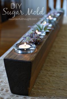 some candles that are sitting on top of a wooden block with succulents in it