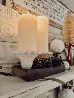 two white candles sitting on top of a mantle