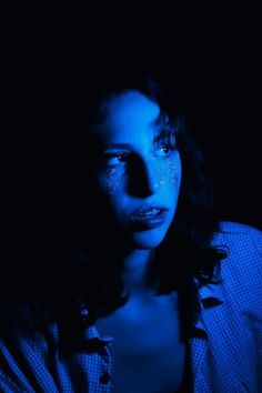 a woman with blue light on her face and body in the dark, staring at the camera