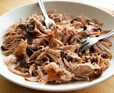 a white bowl filled with shredded meat and two forks