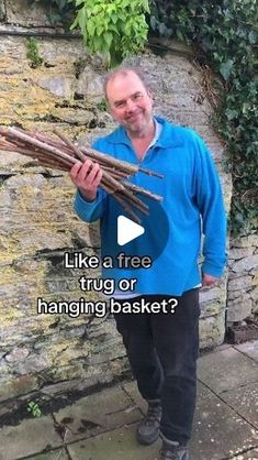 a man standing next to a stone wall holding a bundle of branches in his hands