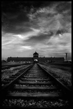 a black and white photo of a train track with clouds in the sky behind it